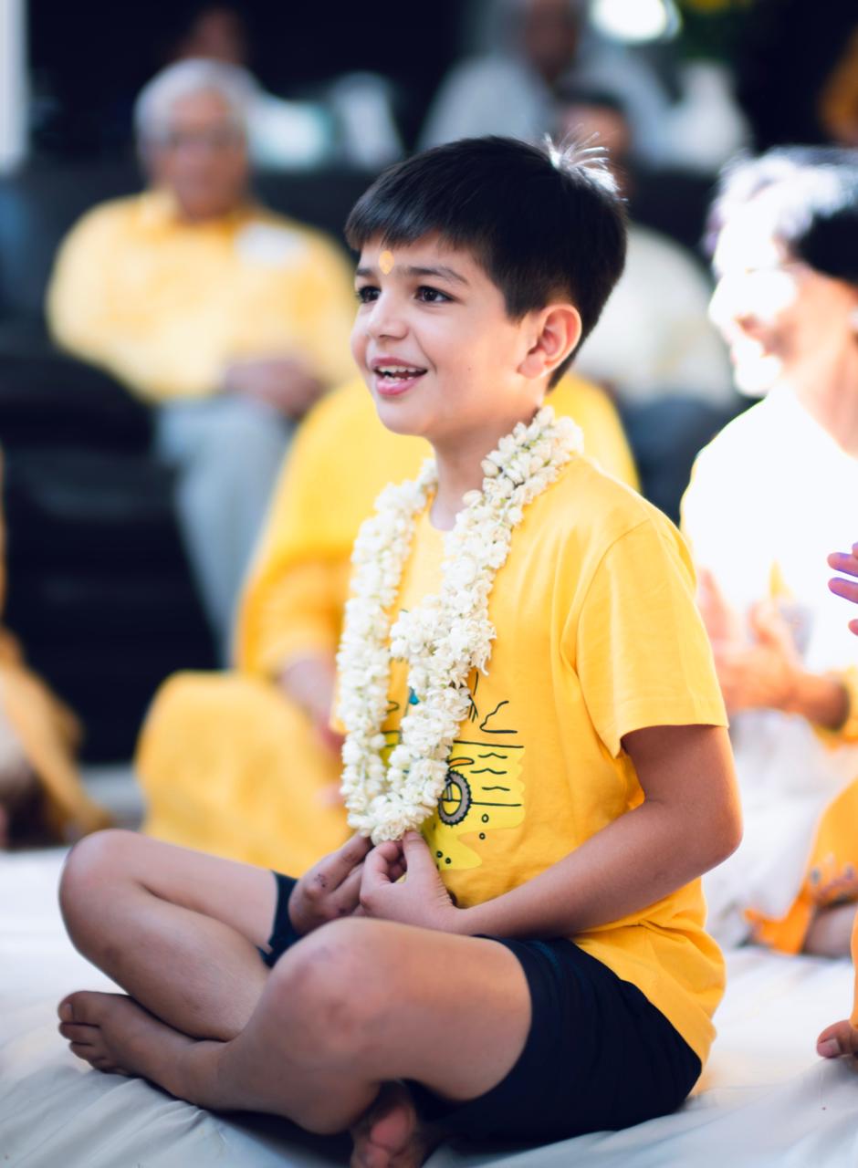 A boy sitting cross-legged, garlanded and smiling